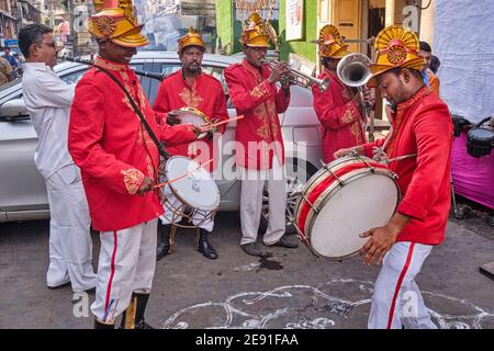 Anlässlich eines hinduistischen Feiertages spielt eine rot-uniformierte Hochzeit- und Festivalband vor einem Hindu-Tempel in Fanaswadi, Bhuleshwar, Mumbai, Indien Stockfoto