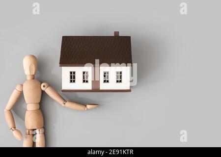 Holzfiguren und Hausmodell auf grauem Hintergrund Stockfoto