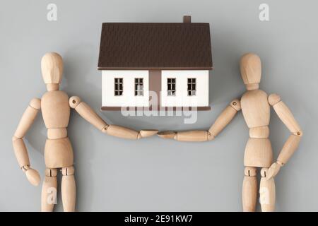 Holzfiguren und Hausmodell auf grauem Hintergrund Stockfoto
