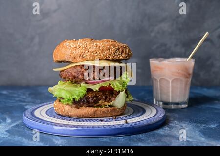 Tablett mit leckeren Burger und Milchshake auf farbigem Hintergrund Stockfoto