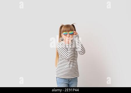 Nettes kleines Mädchen mit stilvollen Sonnenbrillen weht Kuss auf Licht Hintergrund Stockfoto