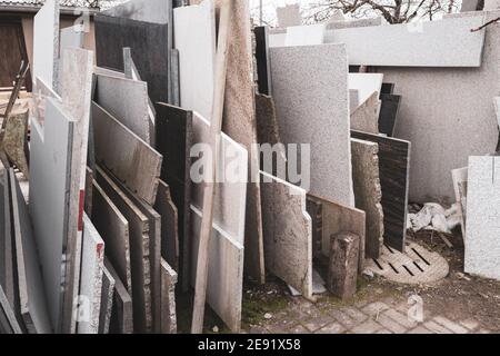 Im Hof einer Steinmetzwerkstatt gibt es viele Verschiedene Granit- und Marmorplatten stehen am Rand daneben Einander Stockfoto