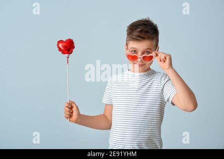 Niedlicher kleiner Junge in stylischer herzförmiger Sonnenbrille und mit Luft Ballon auf grauem Hintergrund Stockfoto