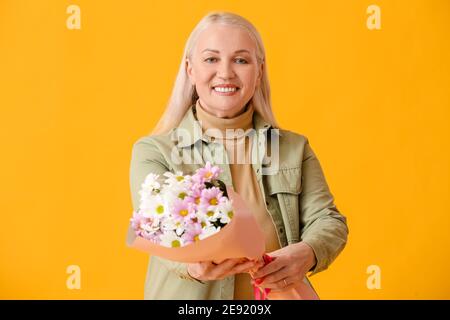 Reife Frau mit Blumenstrauß auf farbigem Hintergrund Stockfoto