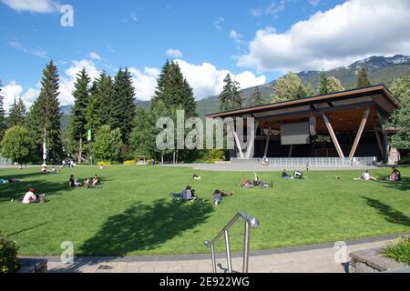 Whistler, Kanada - Juli 5,2020: An einem sonnigen Tag sitzen die Menschen auf der grünen Wiese im Whistler Village mit Bergen im Hintergrund Stockfoto