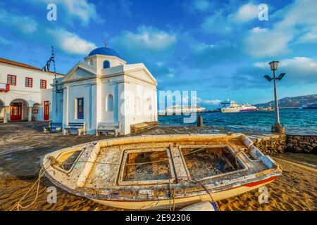 Altes Boot mit griechischer Kirche von Mykonos bei Sonnenuntergang Stockfoto