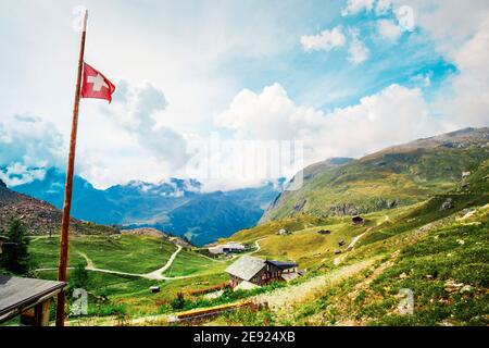 Panoramablick auf die Almwiese mit Gebäuden und schweizer Flagge Stockfoto