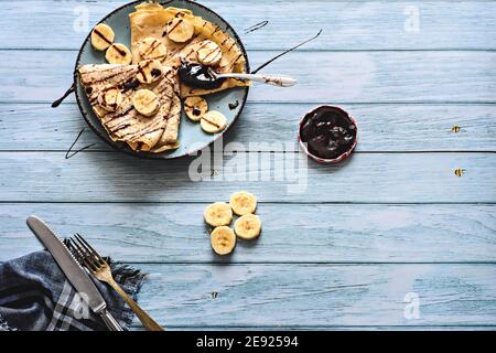 Flache hausgemachte leckere Pfannkuchen mit Bananenscheiben und Schokoladensirup/ Zum Frühstück werden europäische flache Pfannkuchen serviert Stockfoto