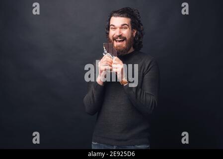 Ein exxzitierter junger bärtiger Mann isst eine Schokolade. Stockfoto