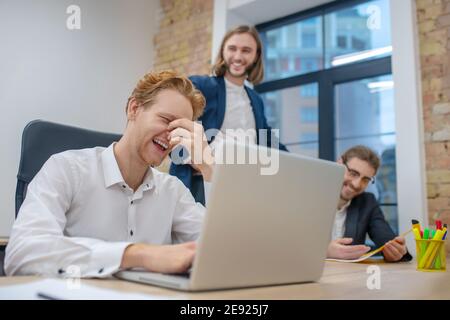 Mann hinter Laptop und Kollegen lustig lachen Stockfoto