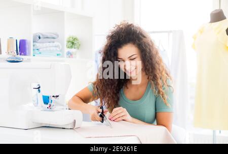 Niedliche Nadelwoman schneiden Stoff mit Schere drinnen Stockfoto