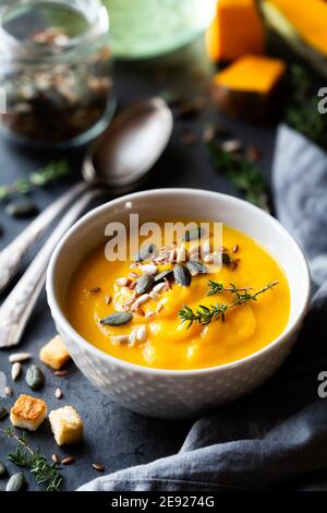 Kürbiscremesuppe in einer Schüssel garniert mit gemischten Samen Und frischer Thymian vor dunklem rustikalem Hintergrund Stockfoto