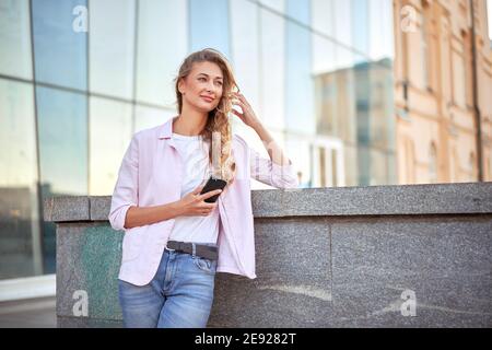 Geschäftsfrau steht Sommertag in der Nähe von Firmengebäude mit Smartphone Zähne Lächelnde Geschäftsfrau im Freien erfolgreiche europäische kaukasische Frau Stockfoto