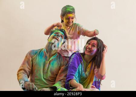 Eltern lächeln ihre Tochter an, während sie Gulal anzieht Sie auf Holi Stockfoto