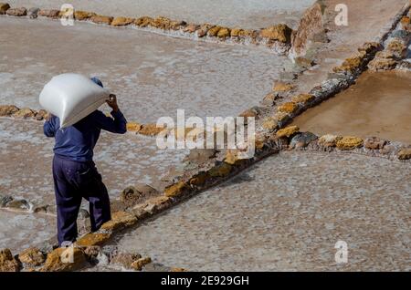 Alter Mann, der einen riesigen Sack Salz auf sich trägt Zurück zu den Salineras de Maras in Peru Stockfoto