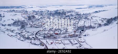 Luftaufnahme des Dorfes Puklice mit Wohngebäuden im Winter. Winterlandschaft schneebedeckten Feld und Bäume in der Landschaft. Tschechische Republik Hoch Stockfoto
