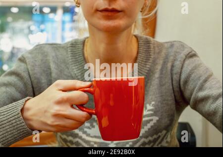 Eine junge Frau in einem grauen Pullover hält eine große Roter Becher Stockfoto