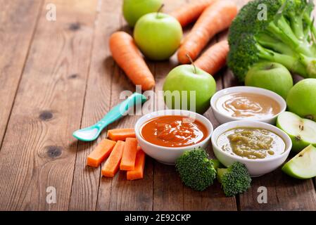Babynahrung. Verschiedene Schüsseln Obst- und Gemüsepüree mit Zutaten zum Kochen auf Holztisch Stockfoto