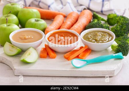 Babynahrung. Verschiedene Schüsseln Obst- und Gemüsepüree mit Zutaten zum Kochen auf Holztisch Stockfoto