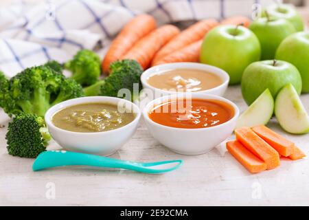 Babynahrung. Verschiedene Schüsseln Obst- und Gemüsepüree mit Zutaten zum Kochen auf Holztisch Stockfoto