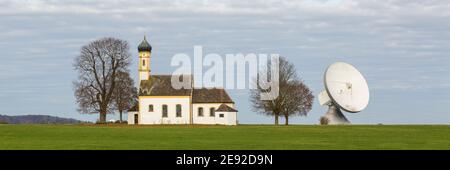 Raisting, Deutschland - 13. Nov 2020: Panorama mit einer Kirche und einer Satellitenschüssel (Radom). Symbiose aus Tradition und Technik. Stockfoto