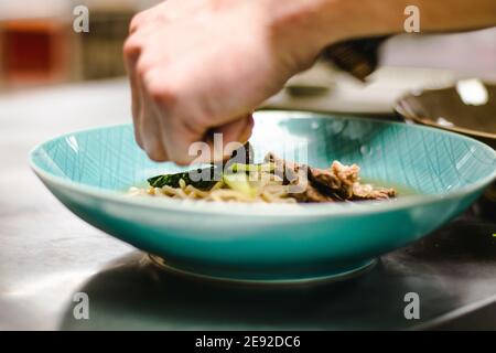 Küchenchef bereitet Ramen-Nudelsuppe mit Fleisch, Eiern und Gemüse in einem Restaurant zu Stockfoto