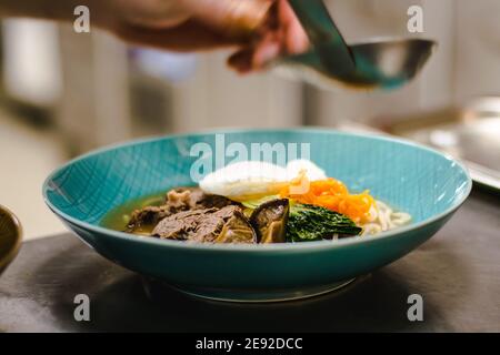Küchenchef bereitet Ramen-Nudelsuppe mit Fleisch, Eiern und Gemüse in einem Restaurant zu Stockfoto