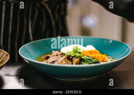 Küchenchef bereitet Ramen-Nudelsuppe mit Fleisch, Eiern und Gemüse in einem Restaurant zu Stockfoto