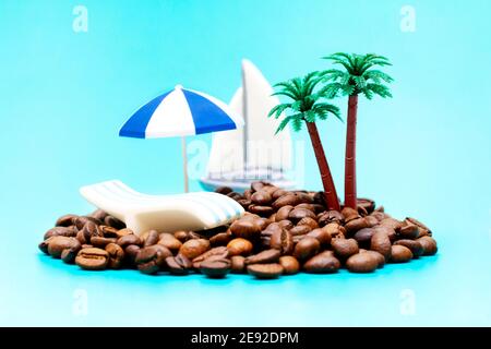 Kreatives, abgelegenes Paradies-Insel-Setup aus gerösteten Kaffeebohnen, Palmen, einem Sonnenschirm und einem unscharfen Spielzeug-Segelboot auf türkisfarbenem Hintergrund im Stockfoto
