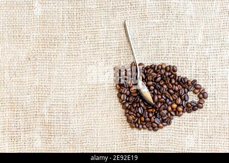 Kreative Anordnung von gerösteten Kaffeebohnen in Form von Ein Becher mit einem Löffel auf einem Sackleinen Tuch Stockfoto