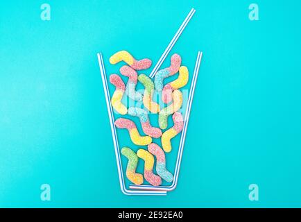Kreative Sommer Cocktail Flat Lay Komposition aus Trinkhalmen Und lebendige zuckerbeschichtete Gummiwürmer auf hellblauem Hintergrund Stockfoto