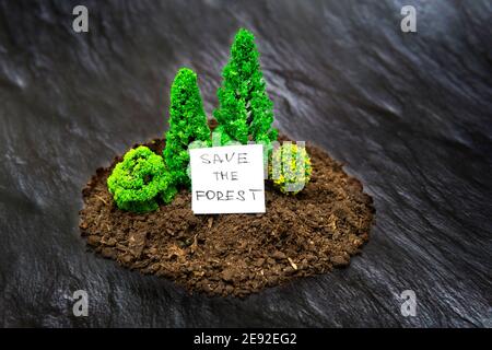 Miniatur Spielzeug Wald Zusammensetzung von einigen Boden und Spielzeug Bäume auf schwarzem strukturierten Hintergrund Imitation verbrannten Land. Konzept „Waldbrände stoppen“. Stockfoto