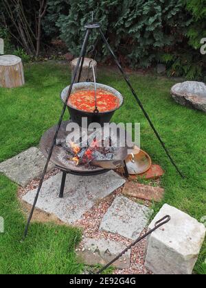 Kessel mit Gulasch auf Stativ über Kamin auf grünem Gras. Gartenparty. Stockfoto