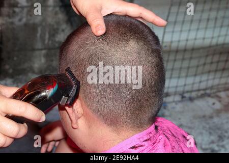 Der Barbier verwendet einen Haarschneider, um dem kleinen Jungen Haare zu schneiden. Stockfoto