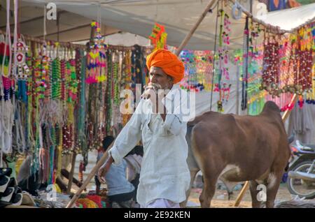 In der Morgensonne sitzt ein Kamelführer auf dem Messegelände. Der orangefarbene Turban auf seinem Kopf ist hell und attraktiv. Stockfoto