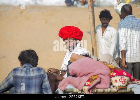 In der Morgensonne sitzt ein Kamelführer auf dem Messegelände. Der rote Turban auf seinem Kopf ist hell und attraktiv. Stockfoto