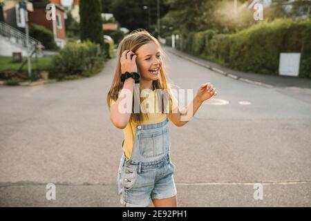 Fröhliches Mädchen mit der Hand im Haar wegschauen, während Sie stehen Auf der Straße Stockfoto