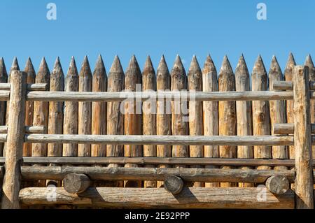 Hoher Zaun aus Holzstämmen auf der Spitze. Alte Pfostenstockade Stockfoto