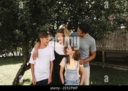 Lächelnde Eltern mit Kindern gegen Baum im Vorgarten Stockfoto