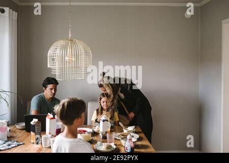 Mutter küsst Tochter über Esstisch zu Hause Stockfoto