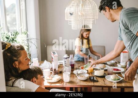 Mutter und Sohn umarmen, während Vater und Tochter stehen Am Esstisch Stockfoto
