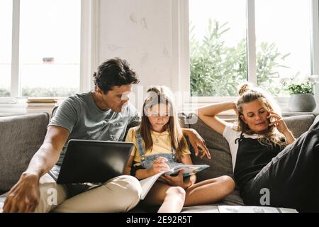 Tochter macht Hausaufgaben sitzen von Mutter und Vater im Leben Zimmer Stockfoto