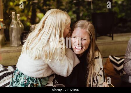 Tochter flüstert etwas ins Ohr der Mutter Stockfoto