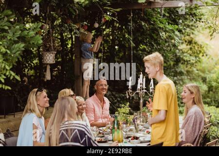 Junge im Gespräch mit der Familie während der gesellschaftlichen Veranstaltung im Hinterhof Stockfoto