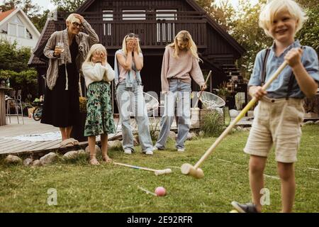 Junge mit Polo-Schläger steht bei der Familie im Hinterhof Am Abend Stockfoto