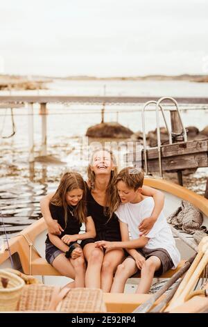 Lächelnde Mutter mit Armen um Kinder, die im Boot sitzen hafen Stockfoto