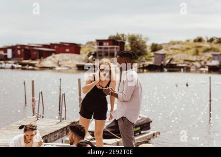 Frau guckt in Mann Telefon von Freunden gegen Hafen während Sommerurlaub Stockfoto