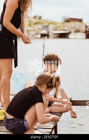 Mittelteil der Mutter stehend, während die Kinder am sonnigen Tag fischen Stockfoto