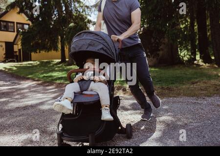 Mittelteil des Vaters, der mit männlichem Kleinkind in der Babykutsche geht Auf der Straße Stockfoto