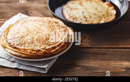 Traditionelle russische Crepes Blini stapelten sich in einem Teller und pfannkuchen in einer gusseisernen Bratpfanne auf dunklem Holztisch. Maslenitsa traditionelles russisches festiva Stockfoto